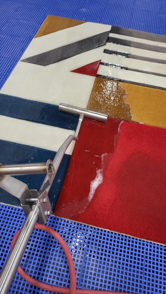 Technician using a squeegee wand to hand-wash a red, navy, and mustard geometric area rug on a raised drainage mat at our Dallas rug-cleaning facility